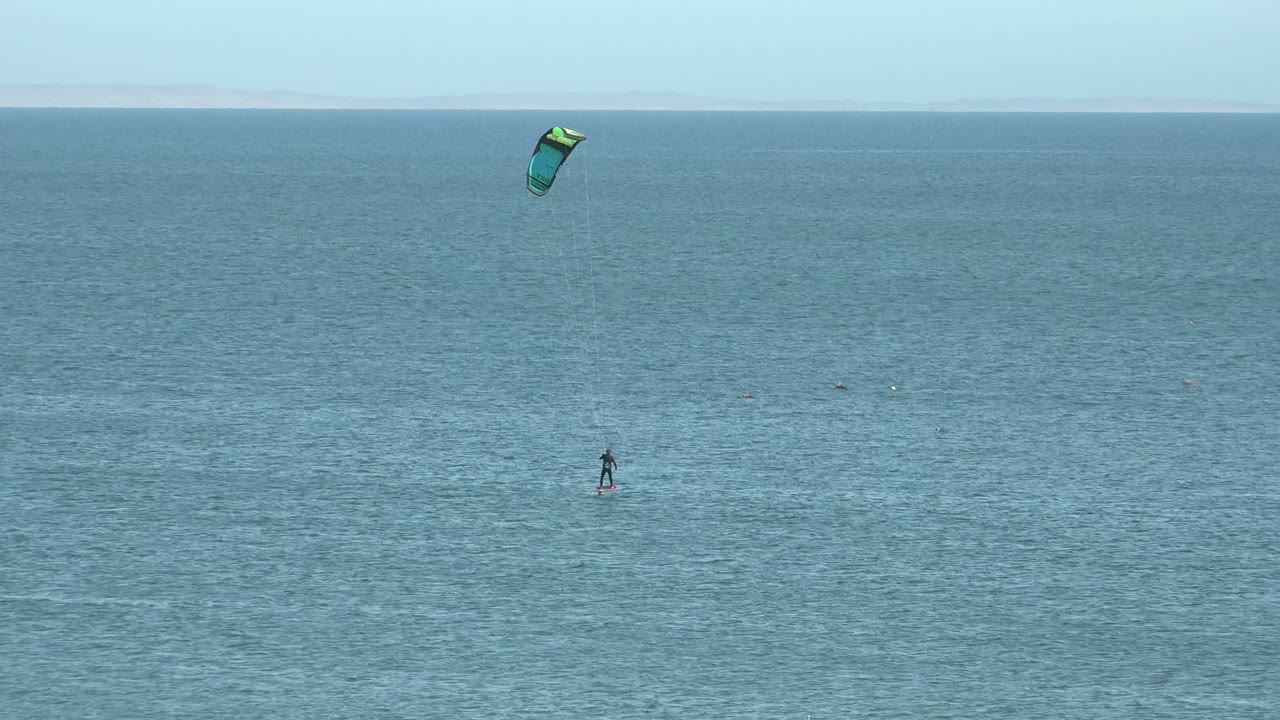 Kite surfer farther right on blue ocean with kite above.