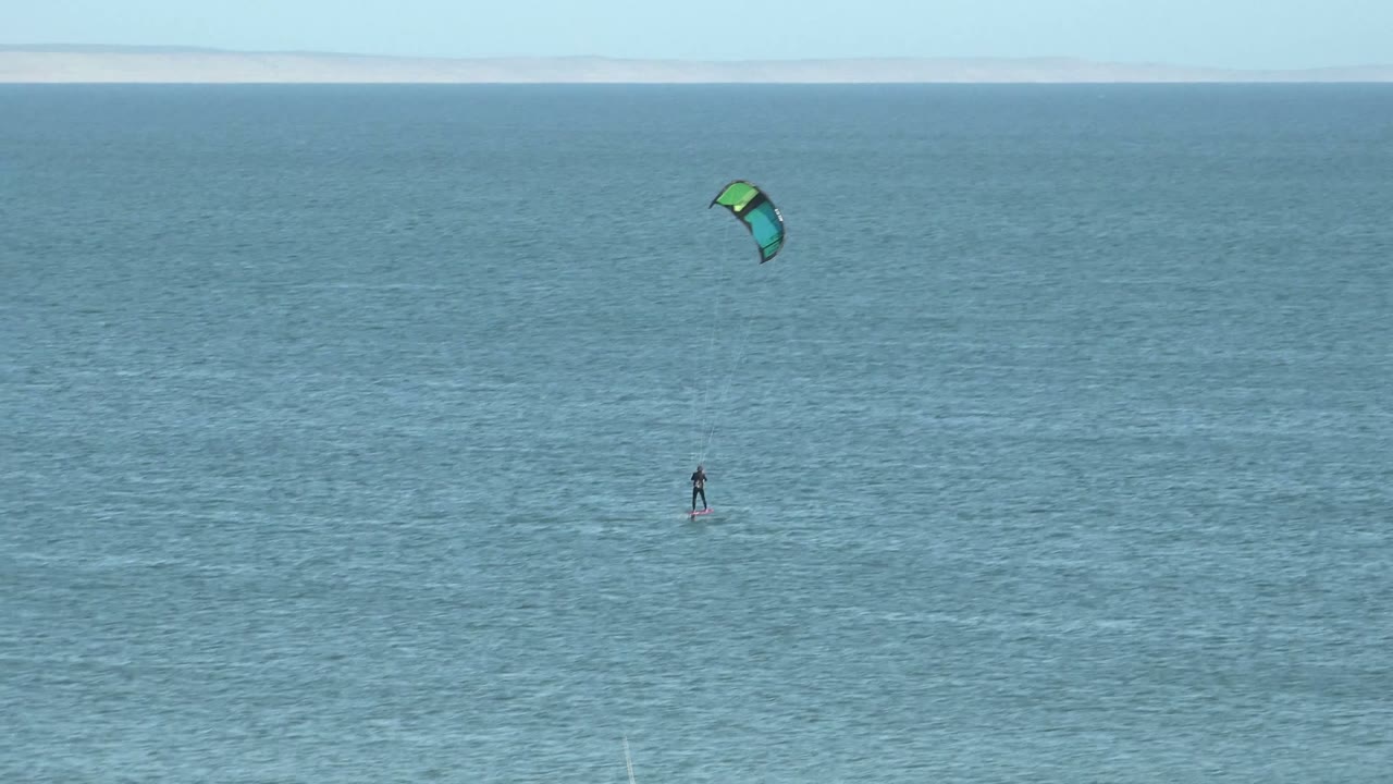 A kite surfer is centered low on the water in San Juanico while the green and blue kite arcs in the upper right area against clear sky.
