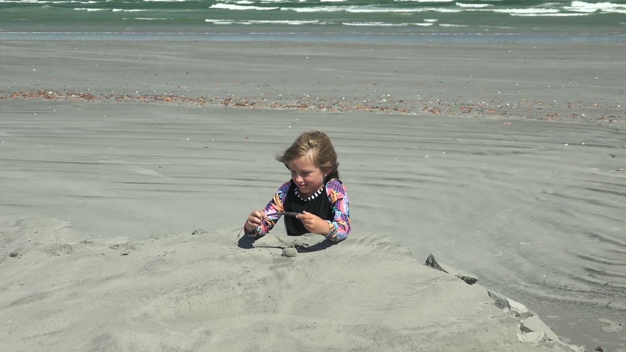 Child holding a small stick while playing in beach sand.