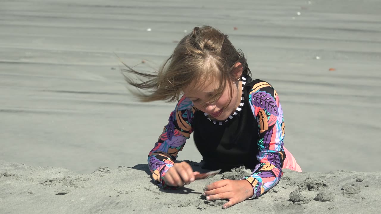 Child looking down while working sand with both hands.