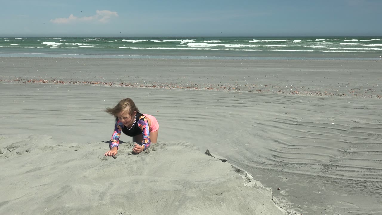 At La Bocana, Mexico, the child leans forward over the sand structure near center frame while rippled beach sand leads toward the ocean.
