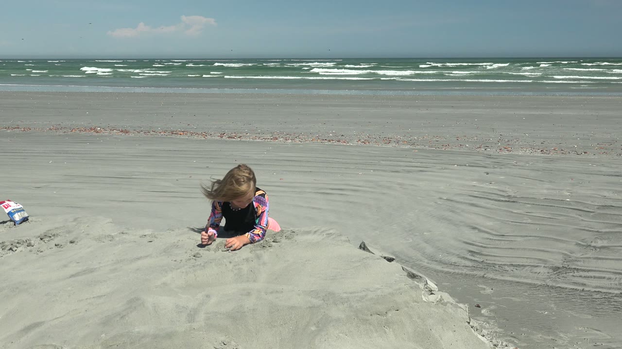 At La Bocana, Mexico, a small toy or bag sits on the sand beside the mound, with the child out of view and the surf stretching across the background.