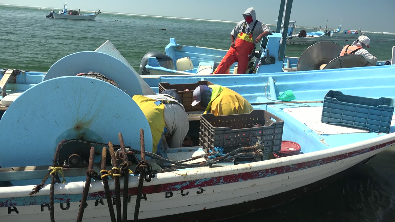 Crew members lean over gear and crates on a fishing boat.