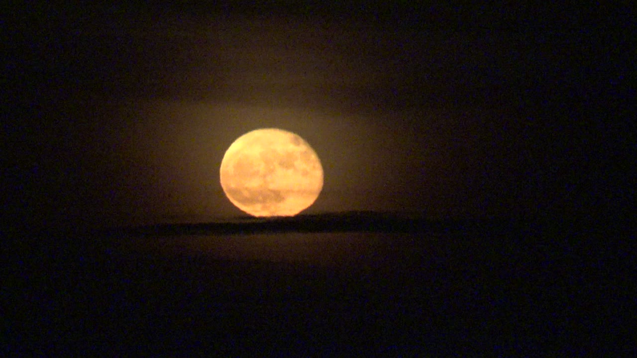 Full moon rising slightly above a black horizon