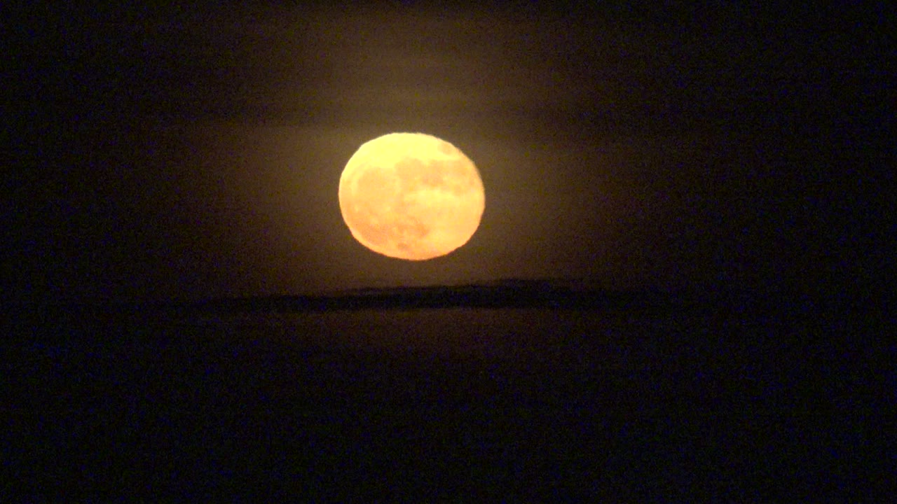 Full moon glowing over a thin dark horizon line.