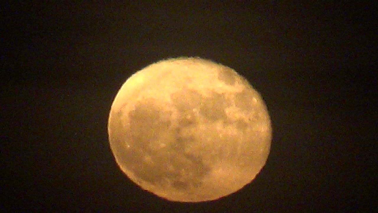 Amber-toned full moon sits in a black La Bocana night sky, with mottled lunar detail visible through a light veil of cloud and no visible people.