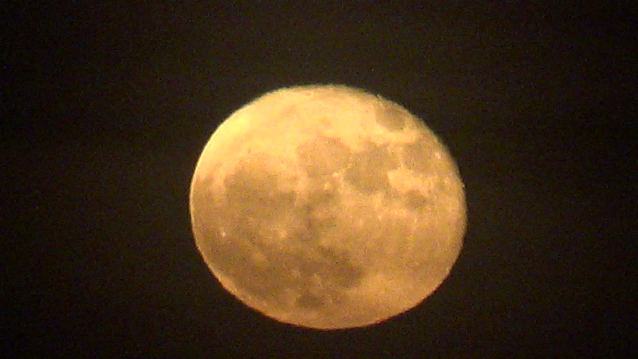 Cratered yellow-orange moon over La Bocana, Baja California Sur, shown against empty dark sky with no ground detail and no visible people.