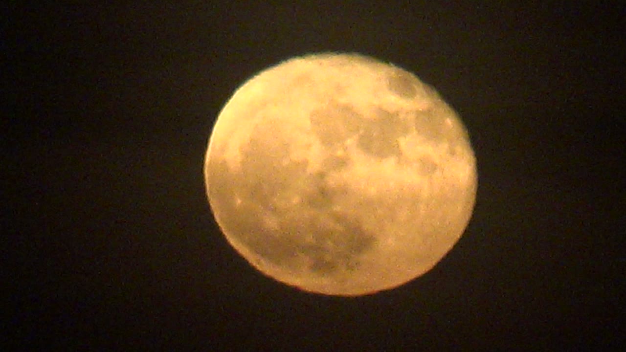 A warm full moon hangs in a dark La Bocana sky as cloud haze softens the top and right side of the lunar disk, with no visible people.