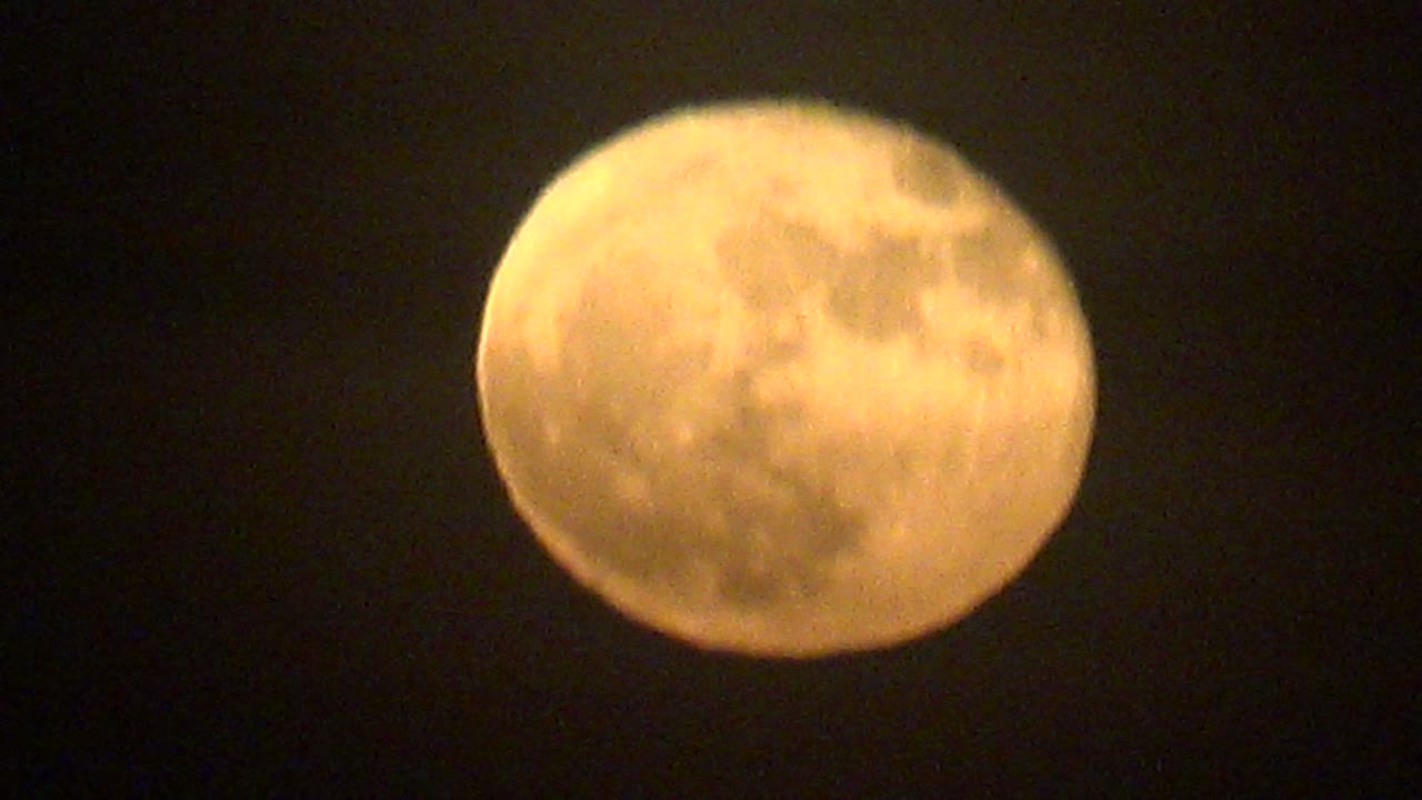 A warm yellow full moon appears high against a dark night sky in La Bocana, Baja California Sur, with faint haze at the moon edge and no visible people.