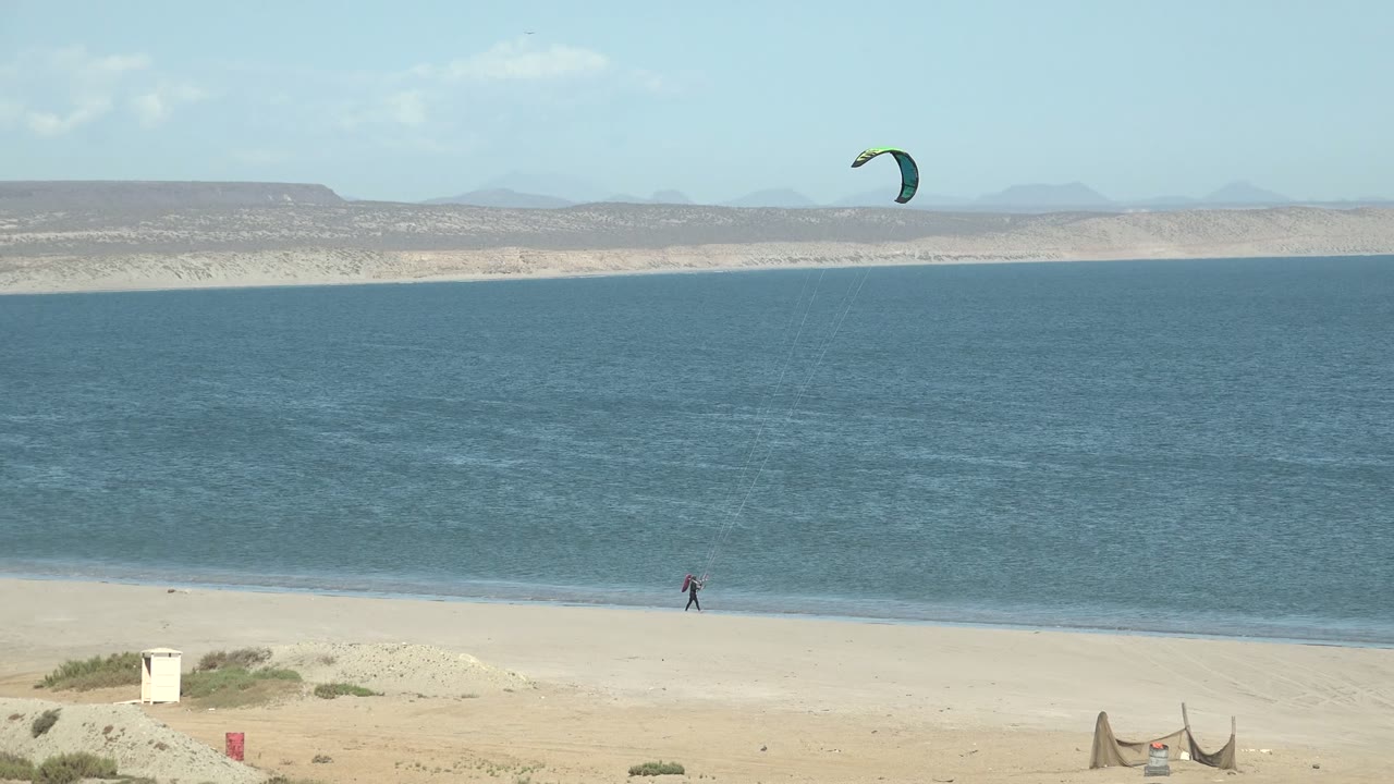 Kite surfer moving along the shoreline under a green kite