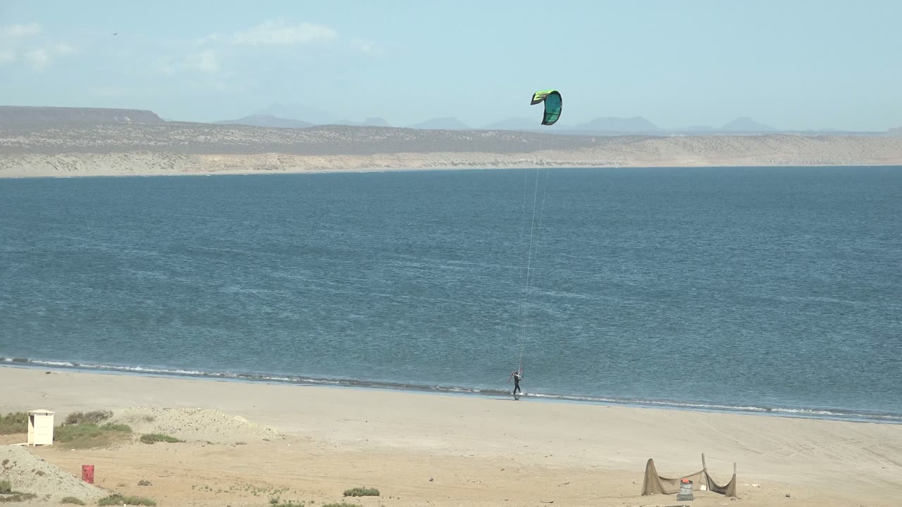 Kite surfer continues along the sandy shore with the kite higher over the water.