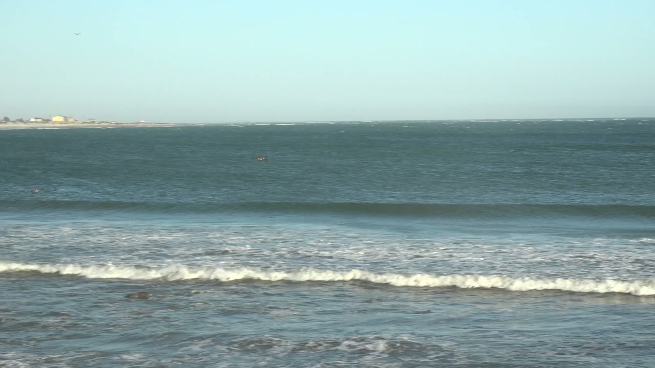 Wide view of ocean waves rolling toward shore in La Bocana, Baja California Sur, with pale blue sky, a distant horizon, white foam, and no visible people.