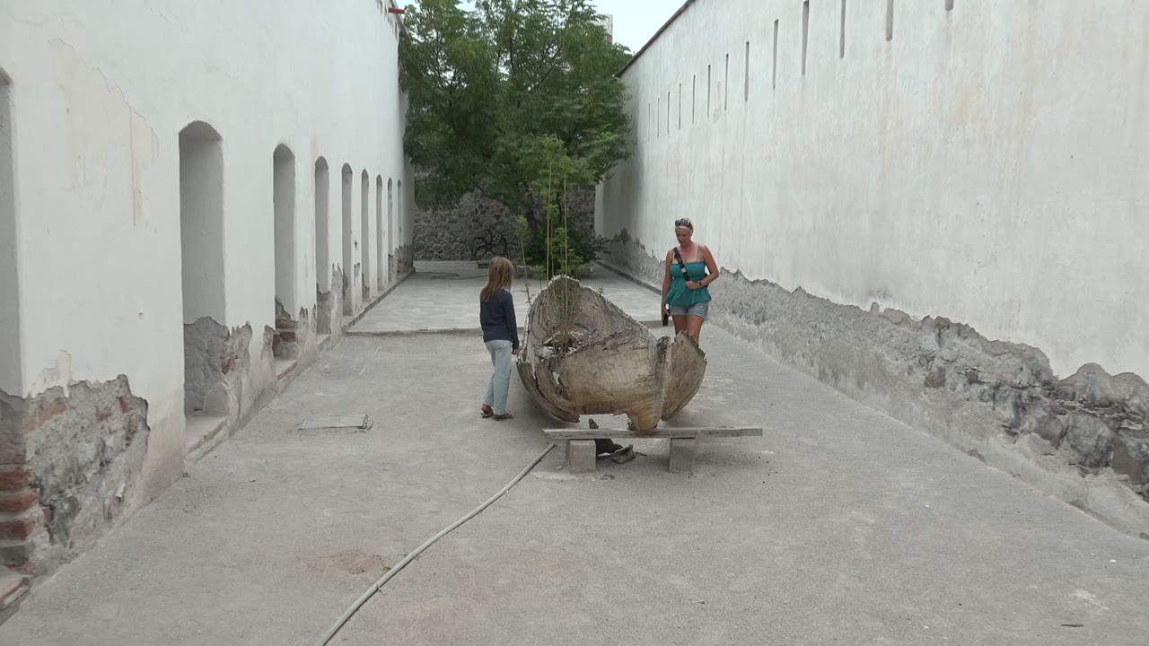 In Mulege, Mexico, a child and adult stand apart near a large shell-shaped sculpture on concrete between white arched walls.