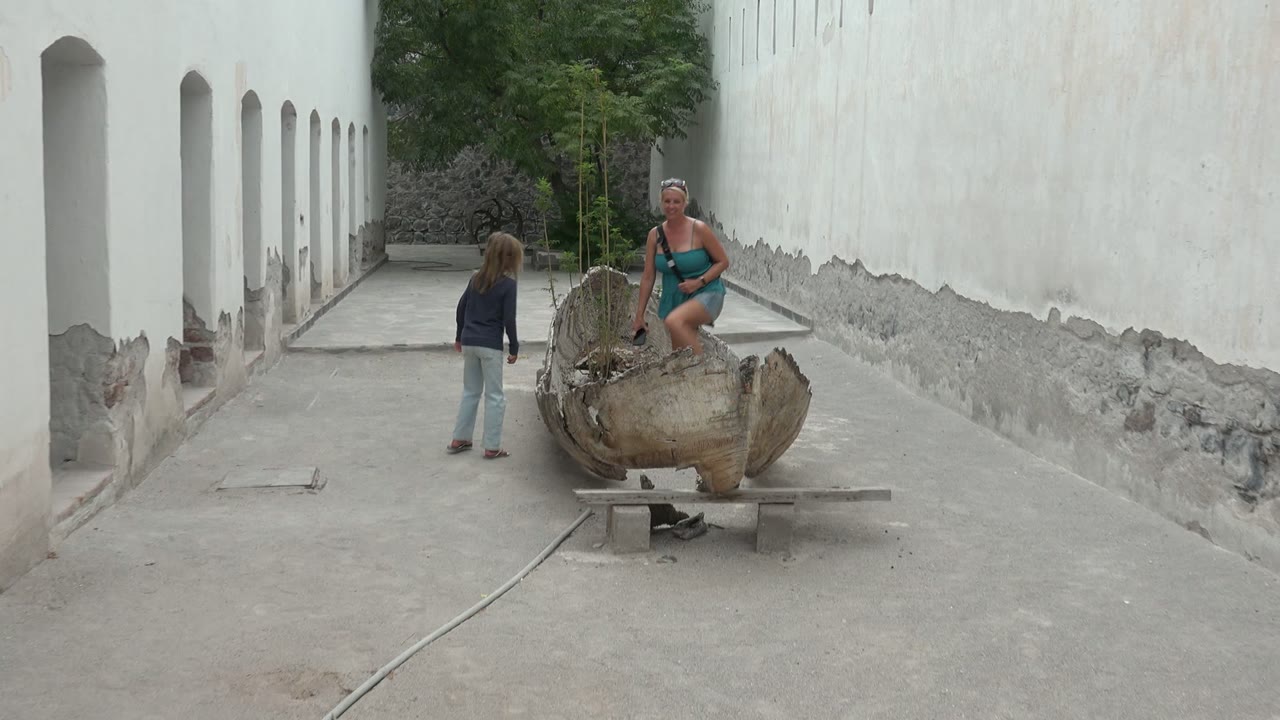 In Mulege, Mexico, the adult starts to step into the shell-shaped sculpture while the child stands nearby in the narrow white-walled courtyard.