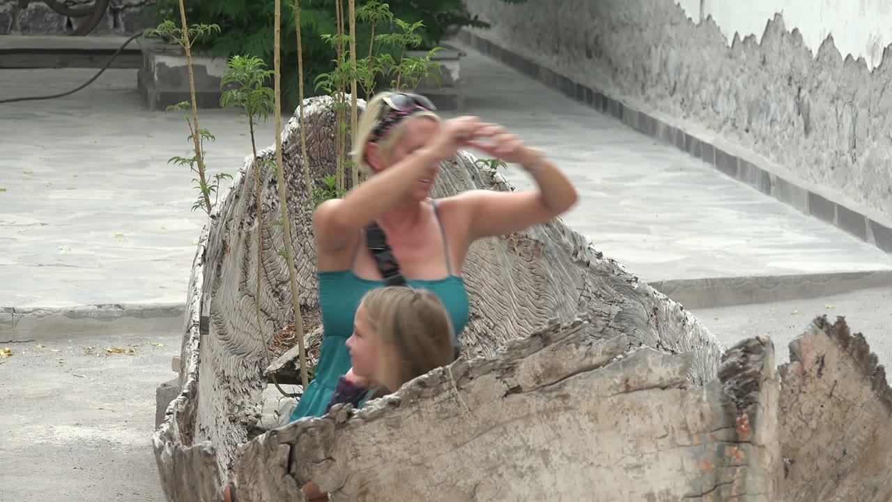 Woman gestures above a child seated in a hollow log structure.