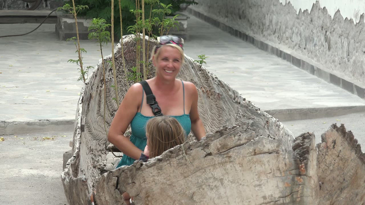 The woman smiles toward the camera while the child sits lower inside the hollow trunk in the outdoor Mulege courtyard.