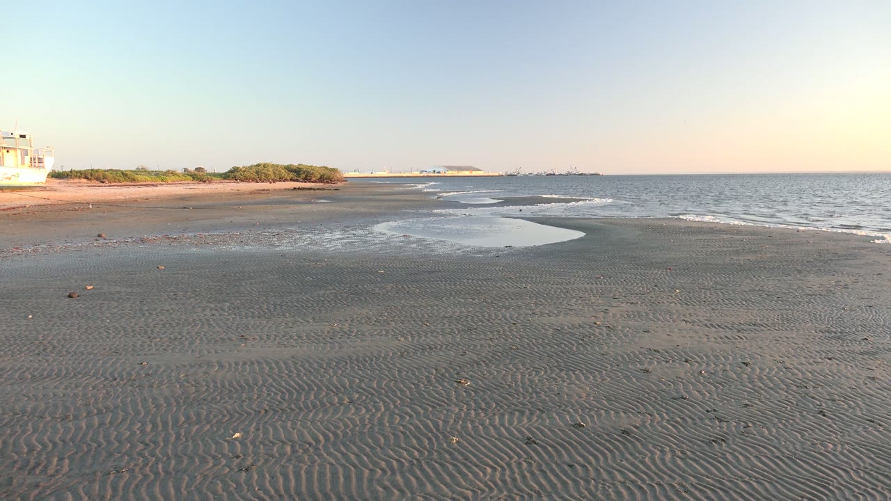 Rippled beach sand and shallow tide water with small waves and the white boat nearly out of frame on the left.