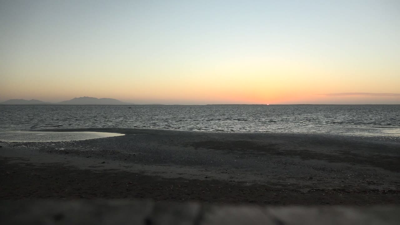 Calm ocean at sunset with dark beach foreground.