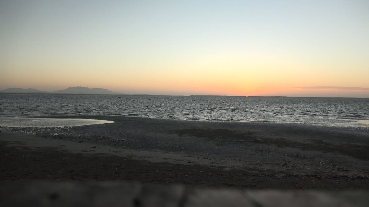 Low sun near the horizon over rippled ocean and wet beach