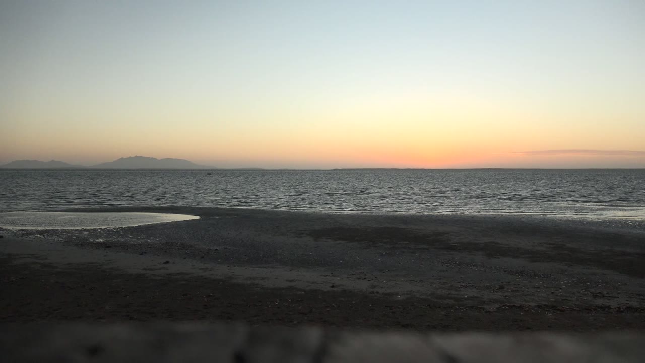 Low waves on a dark beach beneath an orange-blue dusk horizon
