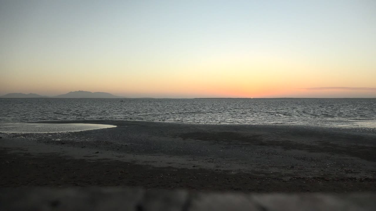 Low ocean waves beyond dark wet beach under a fading sunset sky.