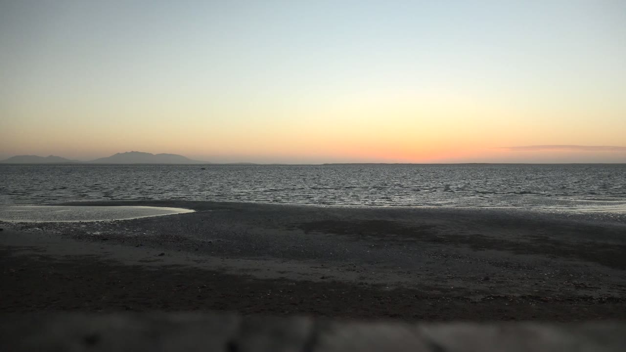 Low beach foreground and calm ocean under a fading orange sky.