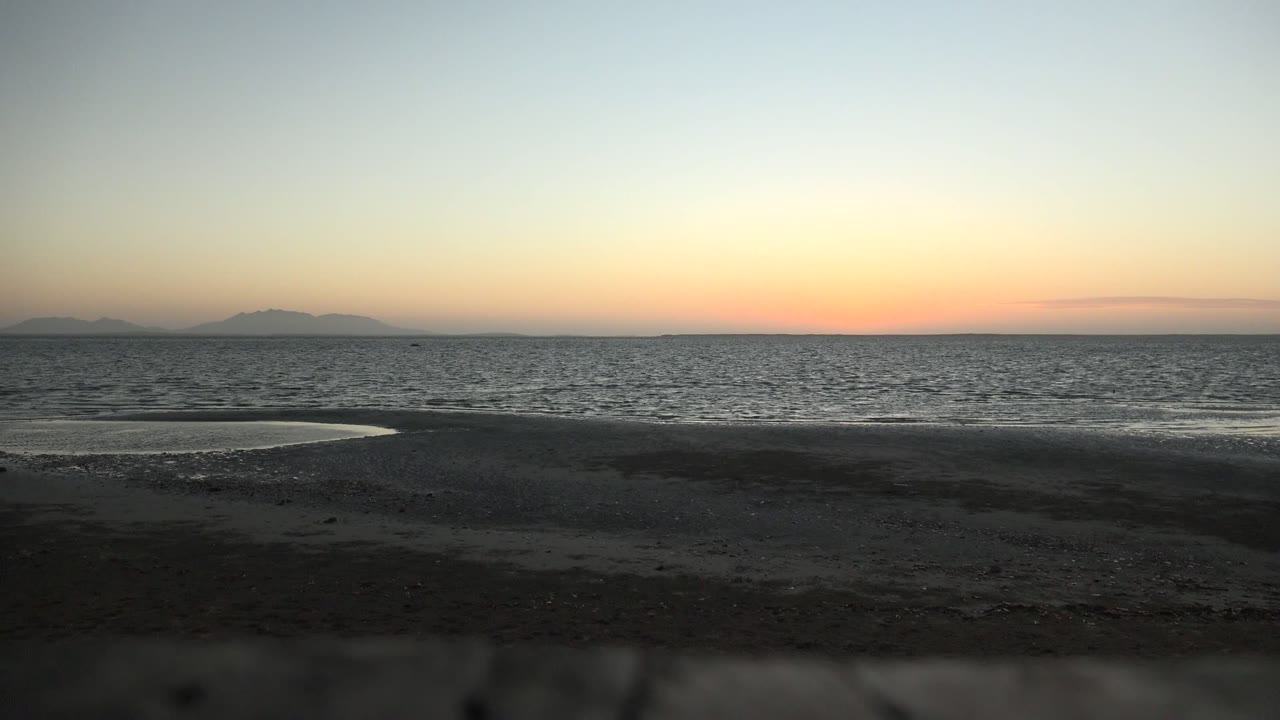 San Carlos, Baja California Sur beach view with a narrow reflective water strip near the shore, textured sea surface, distant islands, and no visible people.