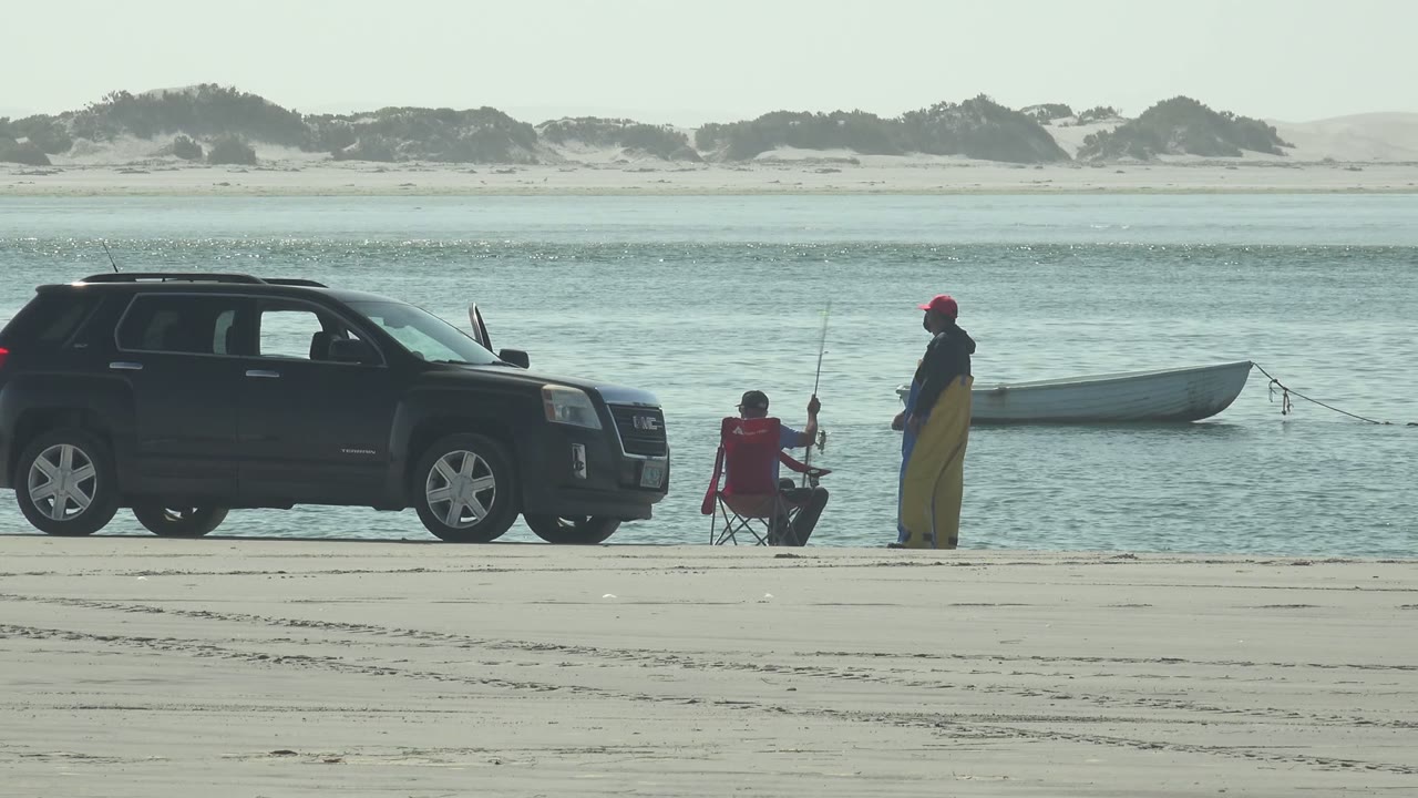 Fishing pair on the beach with SUV and boat near the water.