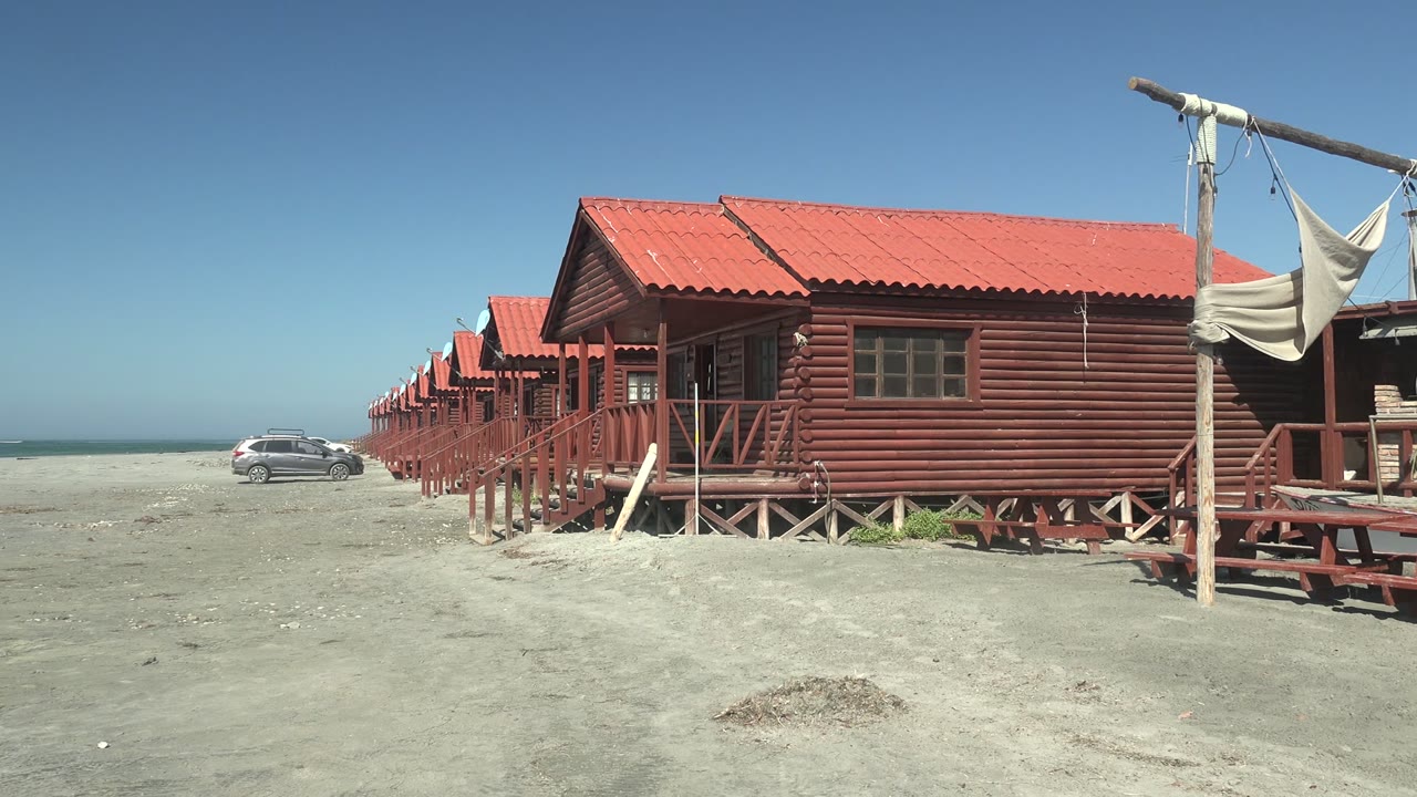 Row of red huts with a parked car near the shoreline.