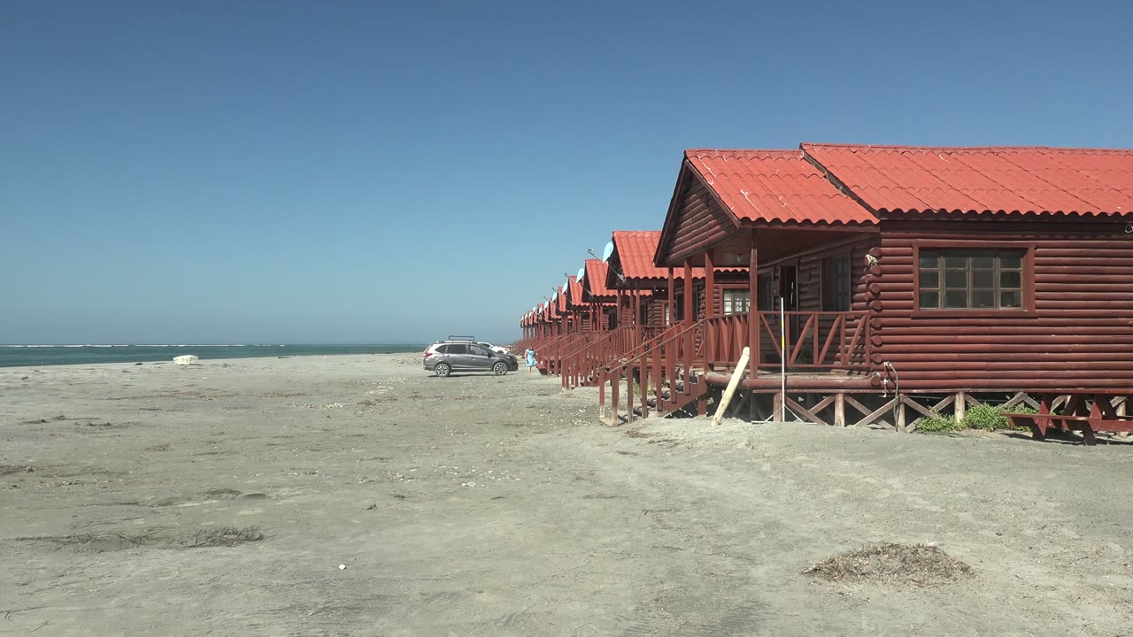 At La Bocana in Baja California Sur, red cabin roofs and wooden railings fill the right edge while the car remains near the ocean to the left, with no visible people.