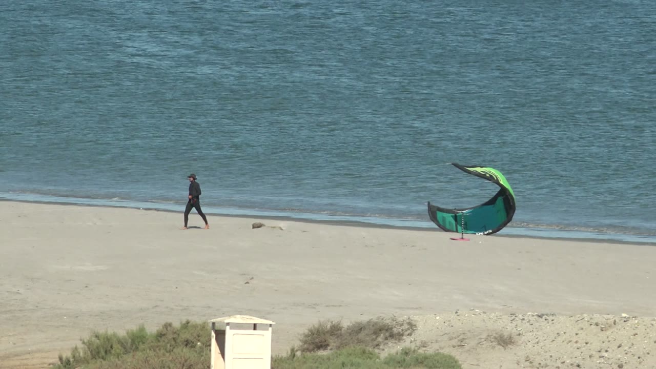 Person farther along the beach near a wind kite by the water
