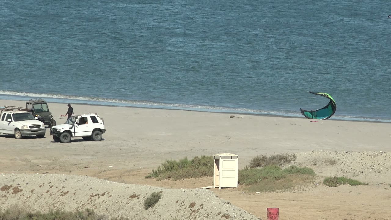 White pickup and SUV on sand with a green kite at the shoreline.