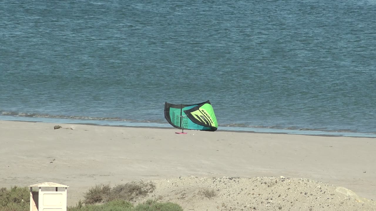 Kitesurfing kite rests on pale sand with ocean water behind it.