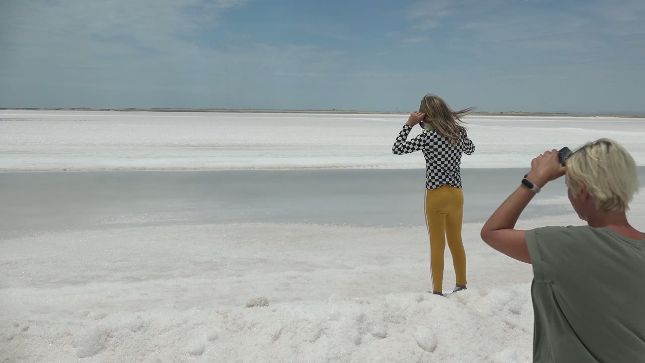 Woman stands on white ground as a blonde man photographs nearby.