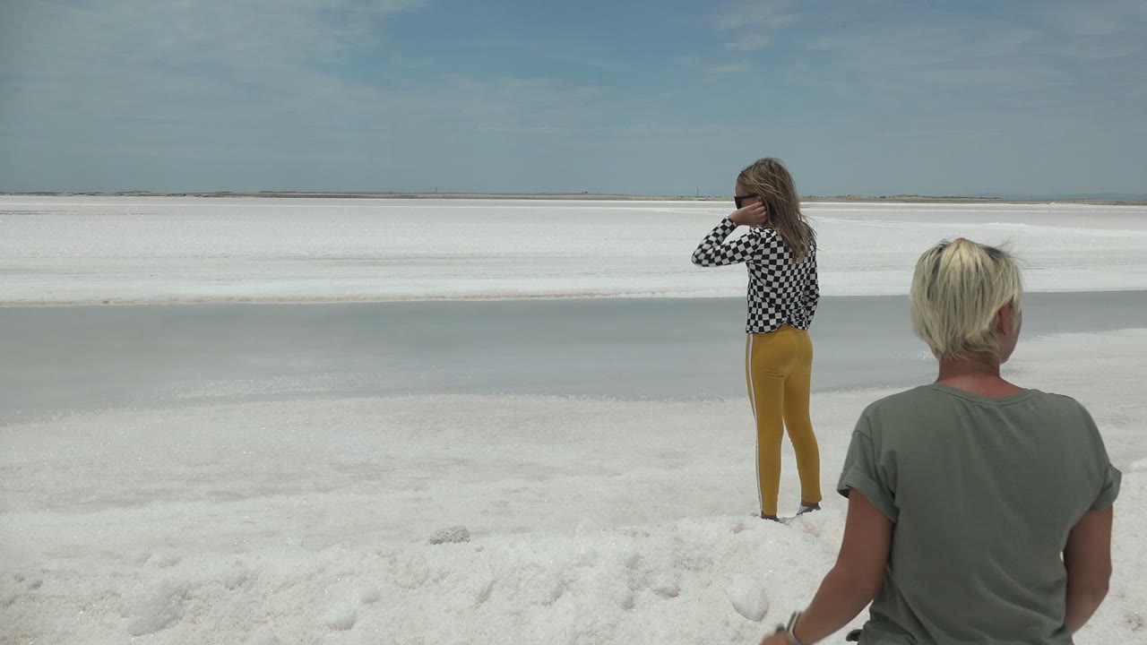 The woman remains near the left midground while the blonde man stands closer to camera on the white landscape in Guerrero Negro, Mexico.