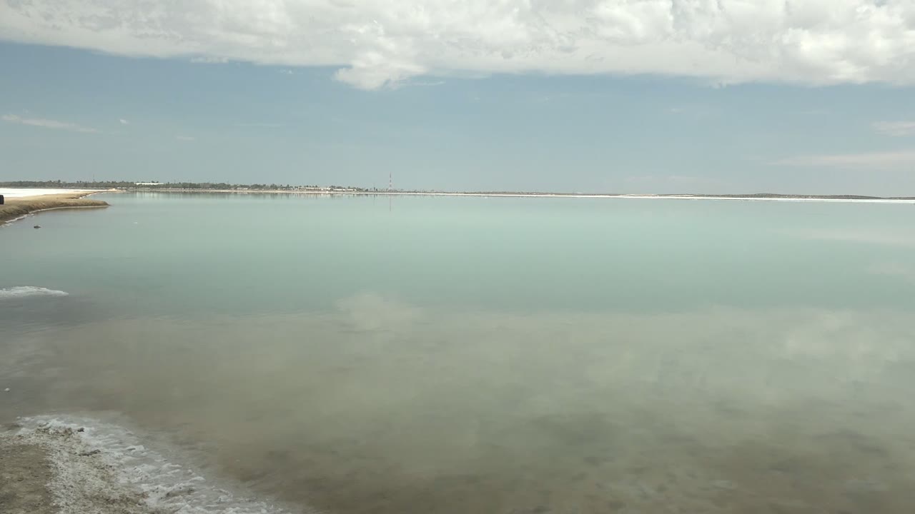 Wide lagoon water with distant shoreline and foam patches near the foreground.