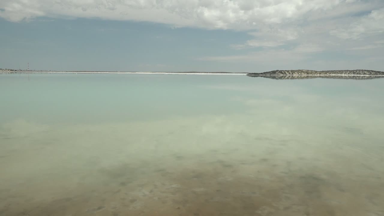 Reflective shallow water and low rocky shoreline beneath a cloudy sky.