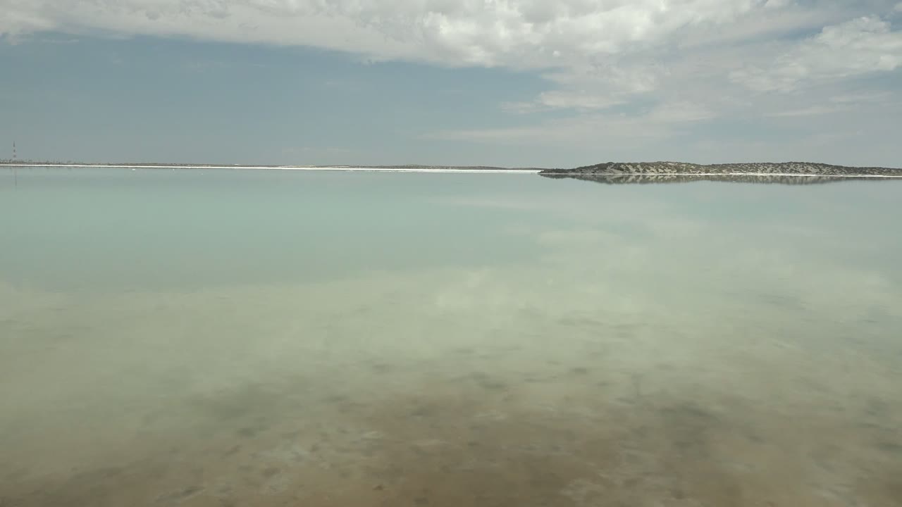 The pan keeps a broad open-water composition in Guerrero Negro, Baja California Sur, with a thin land strip near the horizon, muted cloud reflections, and no visible people.