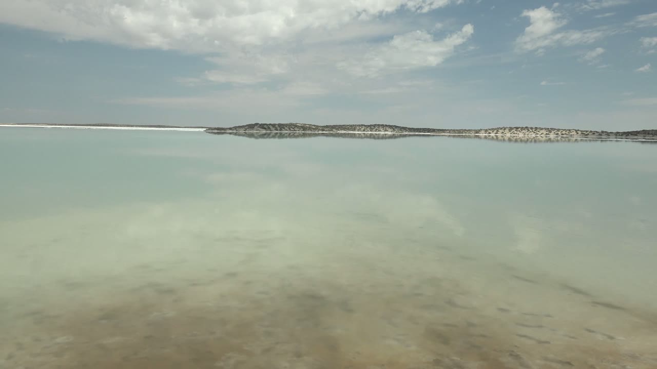 Calm blue-green water under clouds with a thin shore on the horizon.