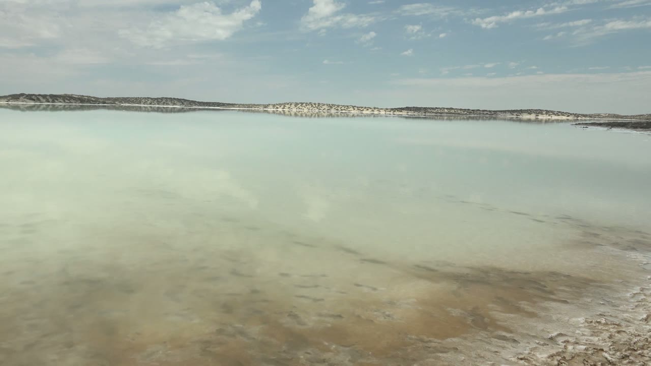 Milky salt lake surface reflecting clouds below a thin horizon.