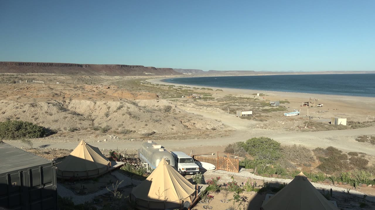 Canvas tents and vehicle above a sandy coastline