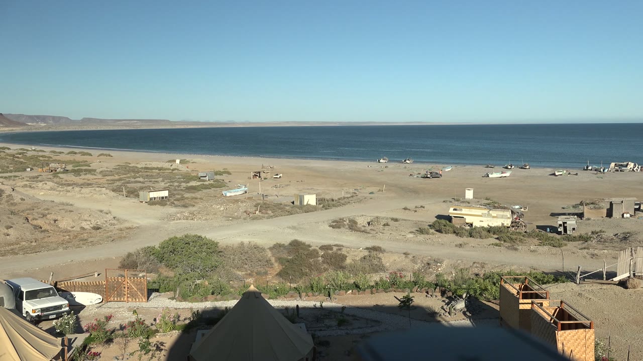 Beach overlook with the van moving leftward below tents and ocean.