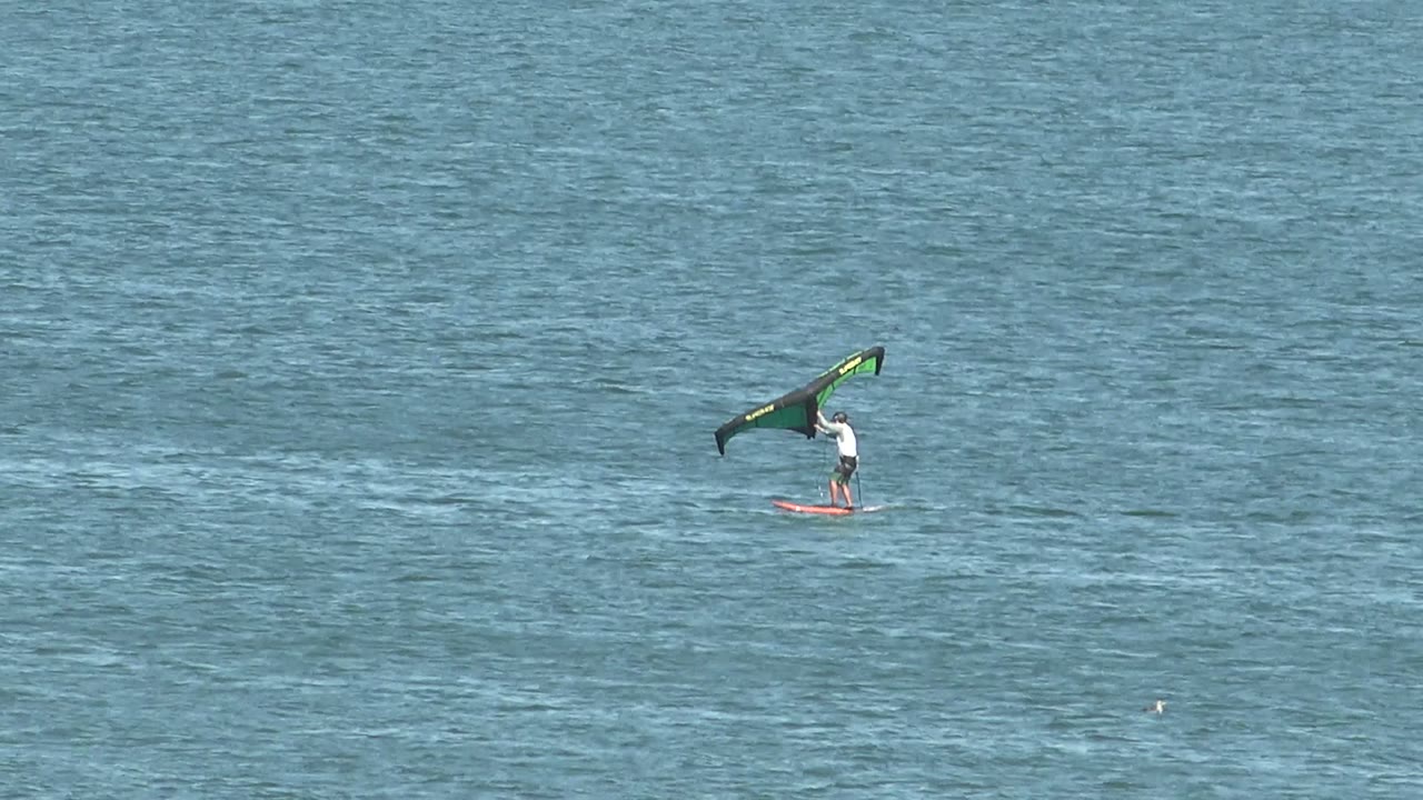 Kite surfer gliding across open blue water with a green and black wing.