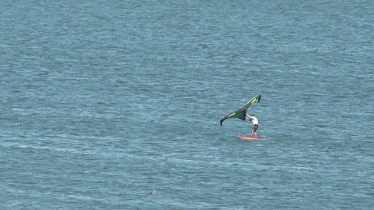 Kiteboarder holding a dark kite over calm blue water.