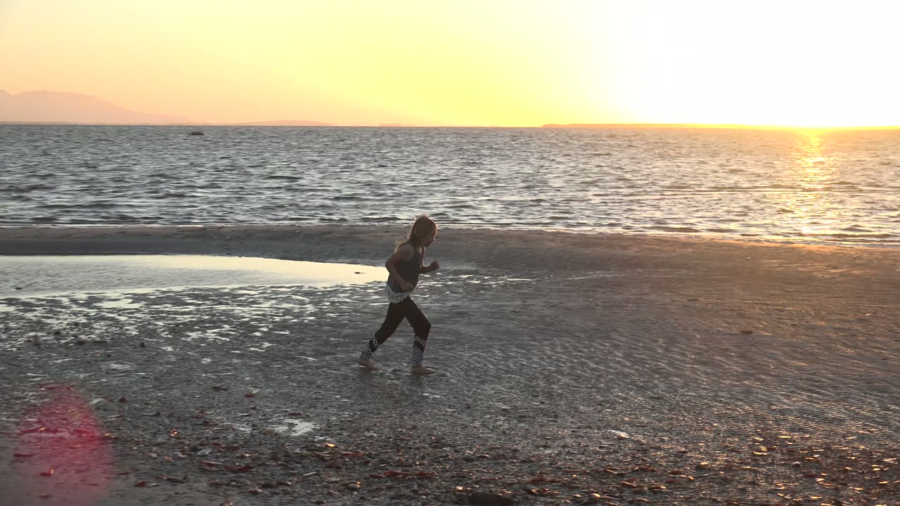A young girl runs along the wet sand in San Carlos, Mexico, with the ocean horizon and bright sunset reflection behind her.