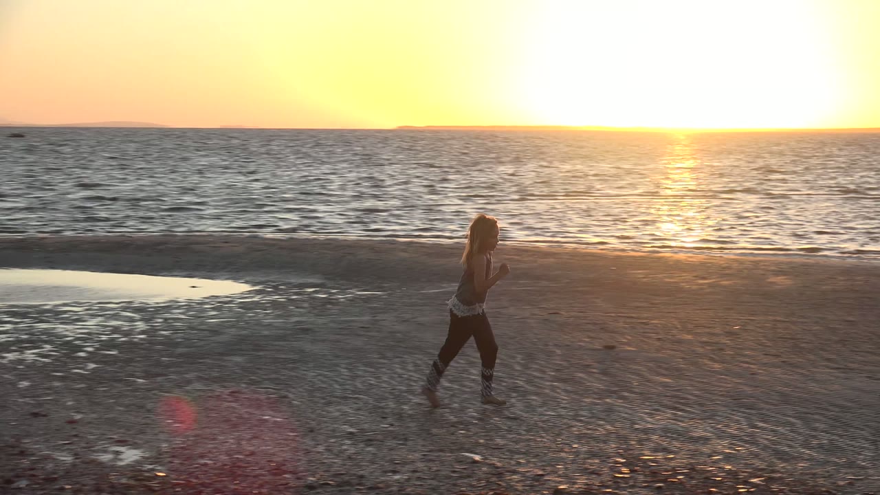 Young girl running across the beach with sunset glare over the water.