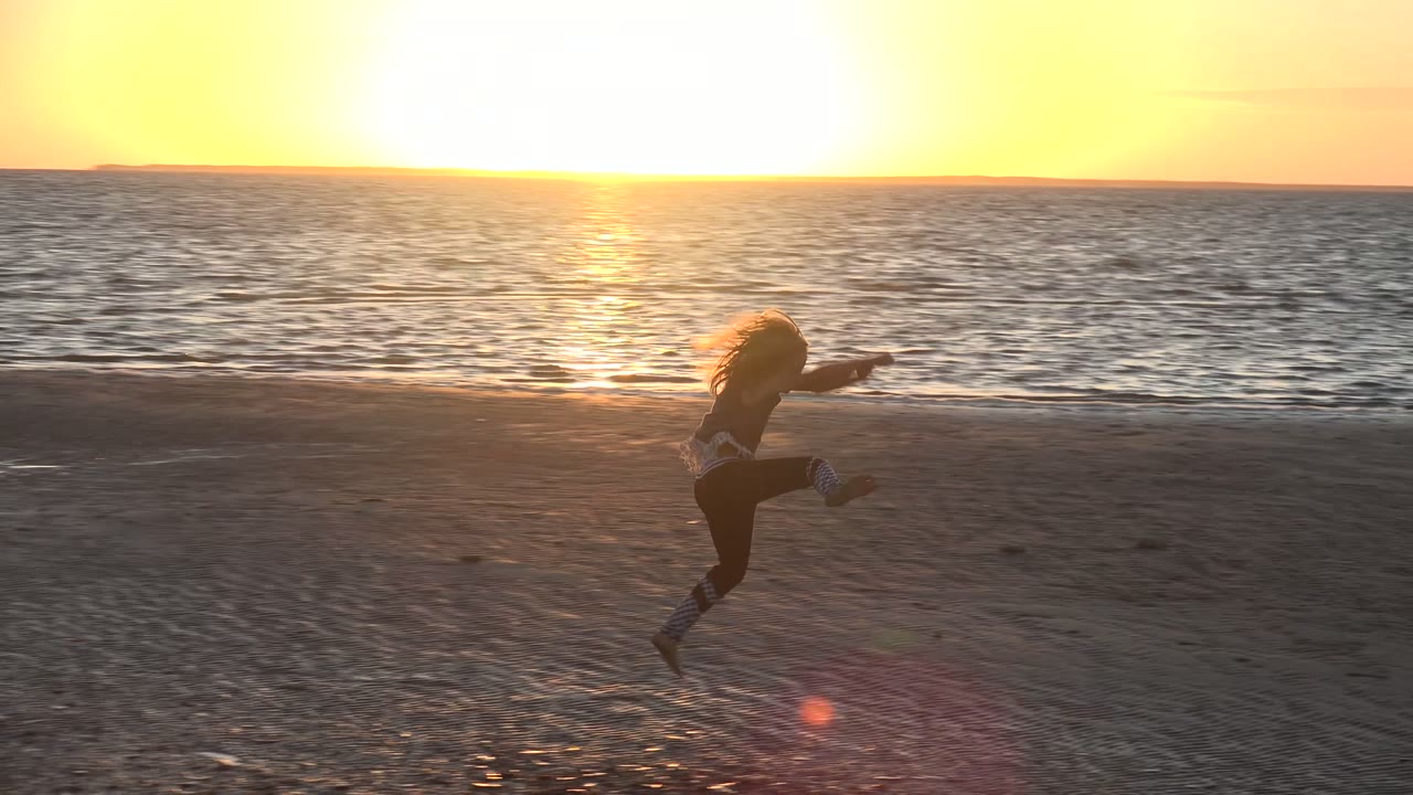 A young girl jumps on the sand in San Carlos, Mexico, silhouetted by low golden light with the ocean stretching across the background.