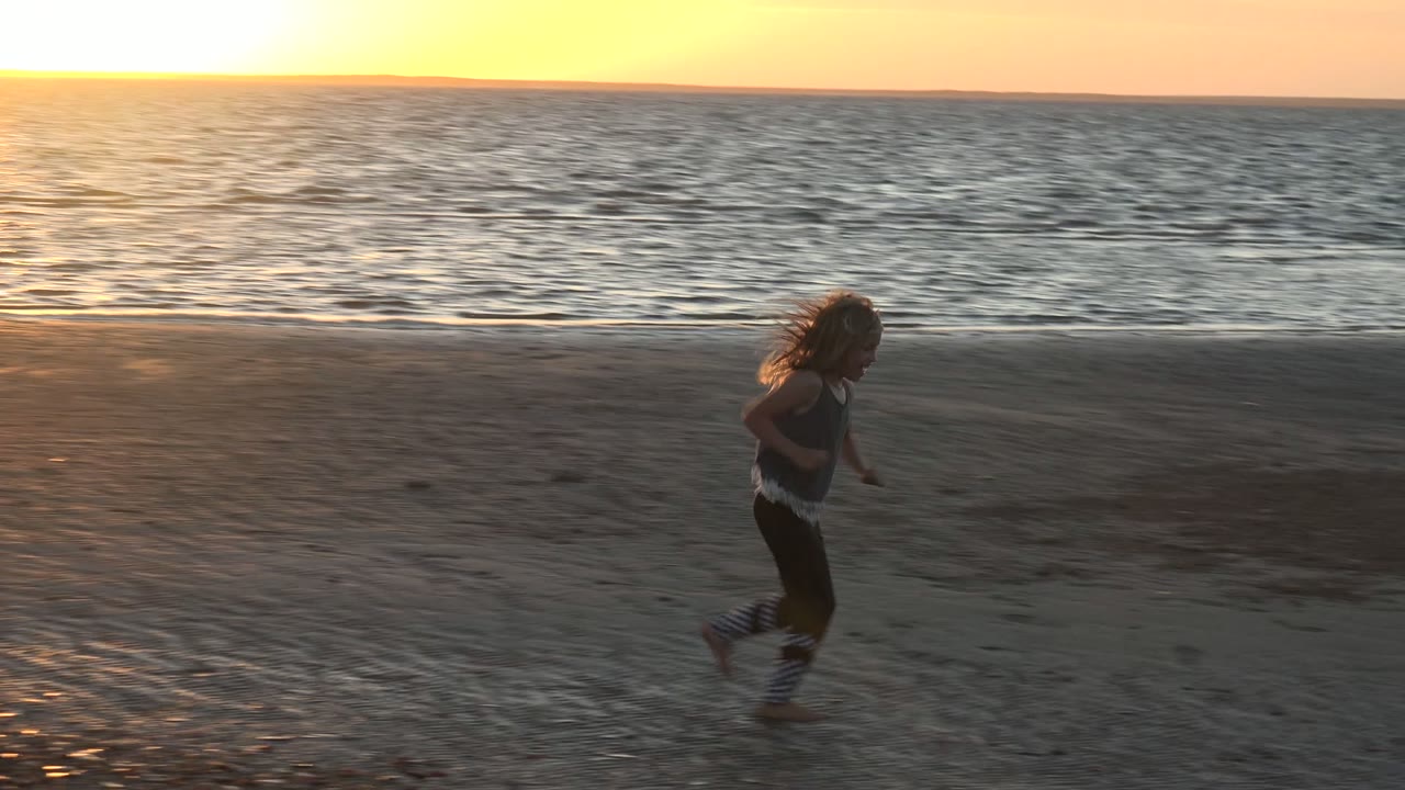 Young girl running near the shoreline with warm sunset light.