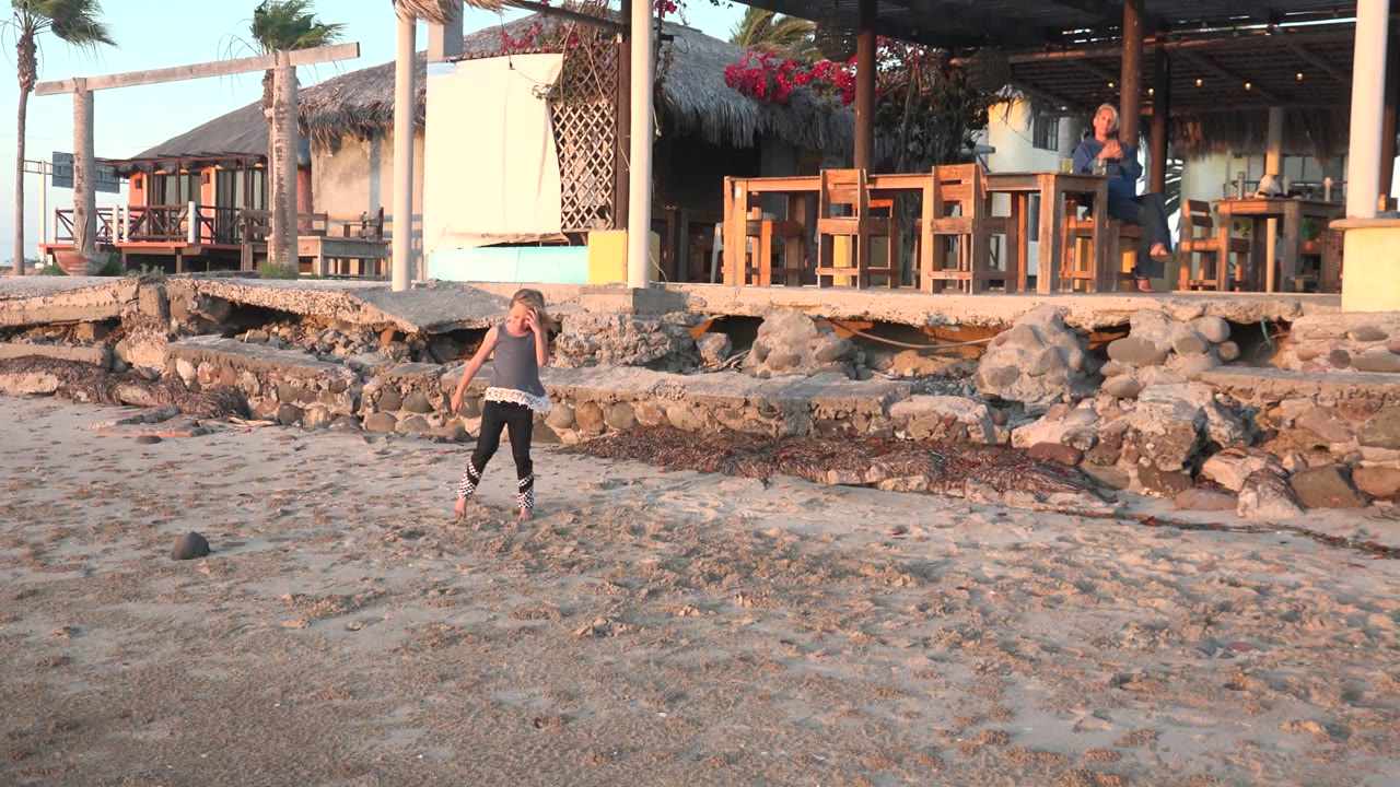 Child farther back on the sand near rocks and a shelter.