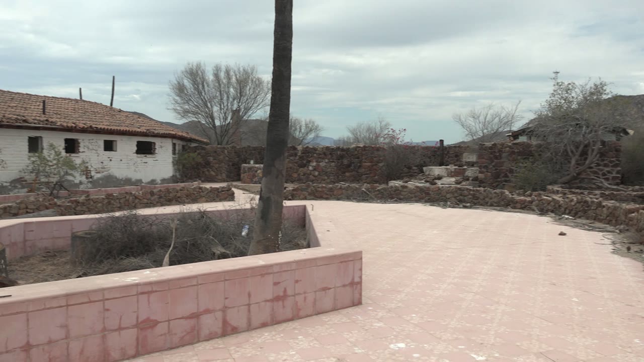 White red-roof building behind stone walls and dry courtyard plants